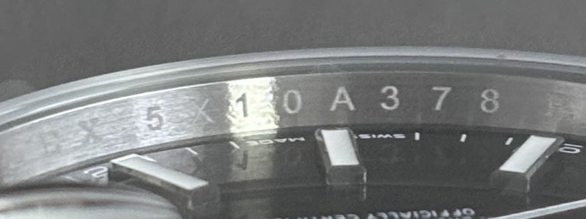 Macro photograph of a Rolex rehaut, the serial number engraved into the inner ring at six o'clock and marked with a box